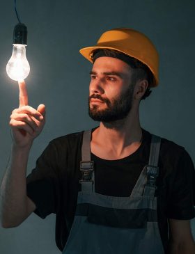 Elektriker mit Schutzhelm hält eine leuchtende LED-Glühbirne in der Hand – Elektrotechnik -Level Up